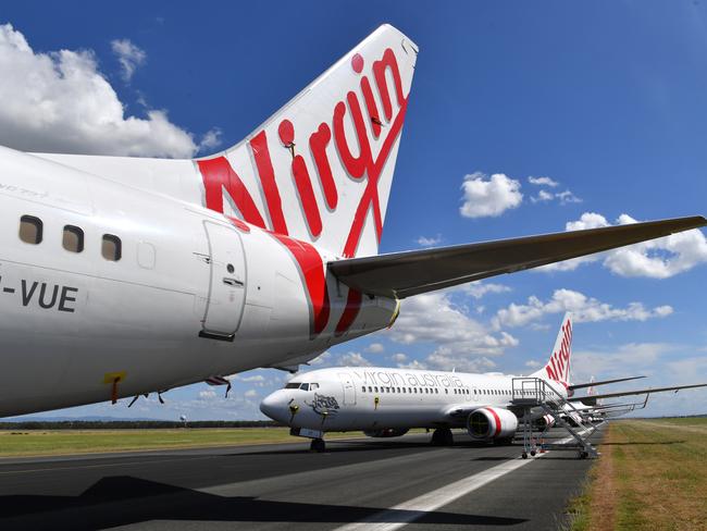 Grounded Virgin Australia aircraft are seen parked at Brisbane Airport in Brisbane, Tuesday, April 7, 2020. Brisbane Airport Corporation (BAC) is working with airlines by accommodating up to 100 grounded aircraft free of charge in response to government-mandated travel restrictions that have grounded a significant proportion of Australia's airline fleet because of the Coronavirus (COVID-19). (AAP Image/Darren England) NO ARCHIVING