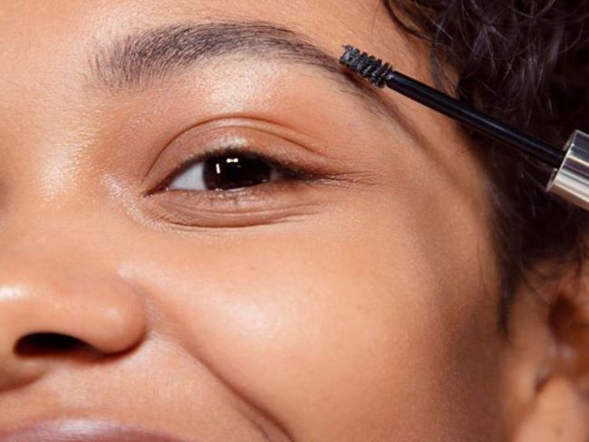 A model applying Glossier Boy Brow eyebrow pomade.