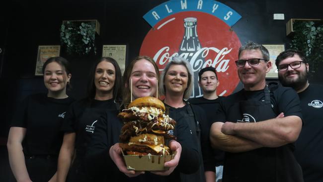 The team at Albury Burger Co – Janita Nickel, Sam Higgins, Amy Jones, Tanya Salvestrin, Alfonzo John, Paul Salvestrin, and Kristian Salvestrin with the Chicken Phukka burger containing four pieces of fried chicken, four pieces of cheese, a pineapple fritter, an egg, bacon, and salad.