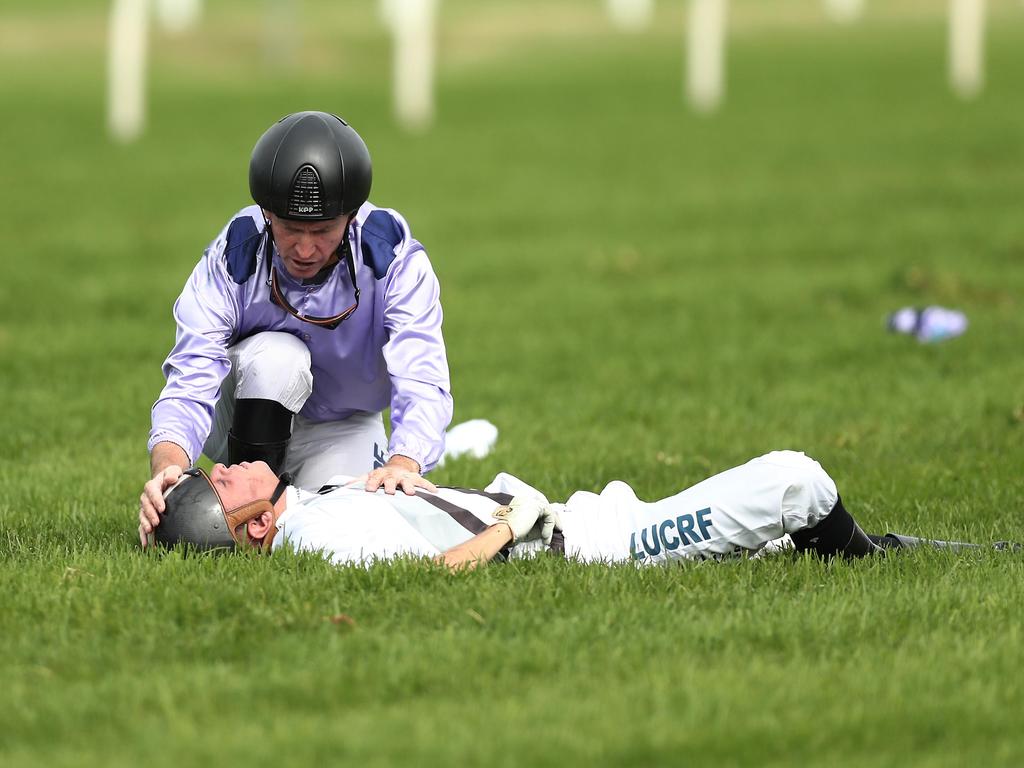 Glyn Schofield, who rode Persan, attends to Andrew Adkins, who was on board War Baron, after they both fell. (Photo by Mark Metcalfe/Getty Images)