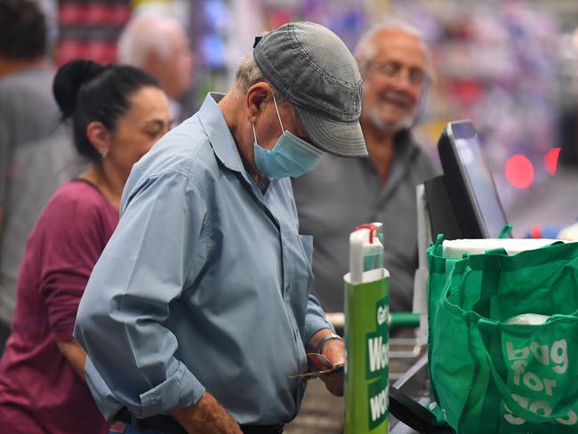 A man wears a face mask as a preventative measure against corona virus at a checkout in a Woolworths supermarket in Coburg, Melbourne, Thursday, March 19, 2020. For a second day, Woolworths has allowed the elderly access to early morning shopping ahead of the general public due to panic buying as Covid-19 fears mount. (AAP Image/James Ross) NO ARCHIVING