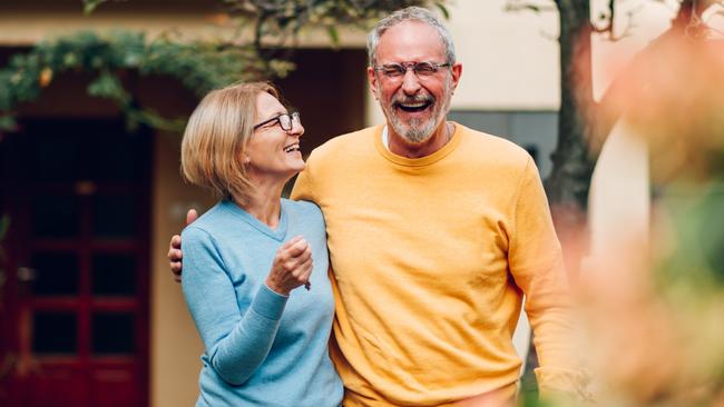 Portrait of a senior married couple holding keys and standing outside their new home on a moving day and hugging. Mature people outside their new house. Copy space. Investing in property.