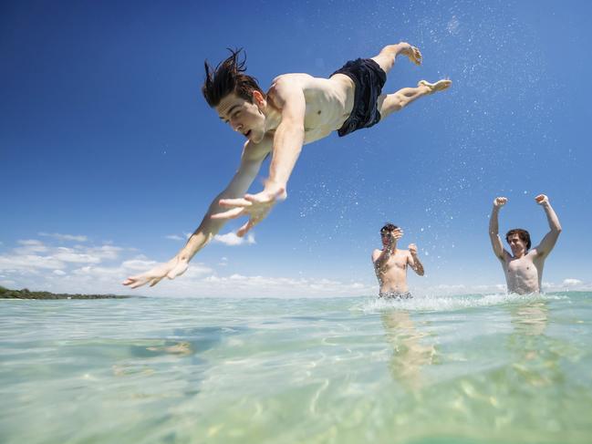 18 year old Noah Behan leaps into the water at Little Cove in Noosa with the help of mates Harry Stiller 17, and Isaac Austin 18, as a heatwave is expected to set in across the state.  Photo Lachie Millard