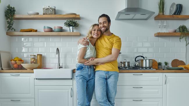 Full length of young couple embracing while standing at the domestic kitchen