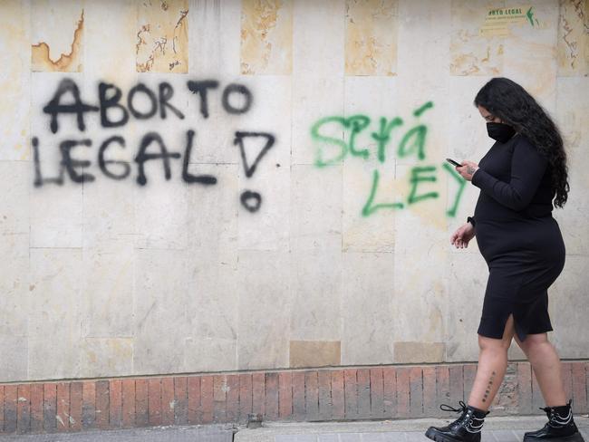 A woman passes by a wall that reads "Legal abortion" and "It will be law", during a demonstration awaiting the decision of the Constitutional Court on it's decriminalization in Bogota, on November 18, 2021. - People against and in favor of free abortion met this Thursday during a day of protest in front of a high court that this week will decide whether to decriminalize this practice in Colombia. (Photo by Raul ARBOLEDA / AFP)