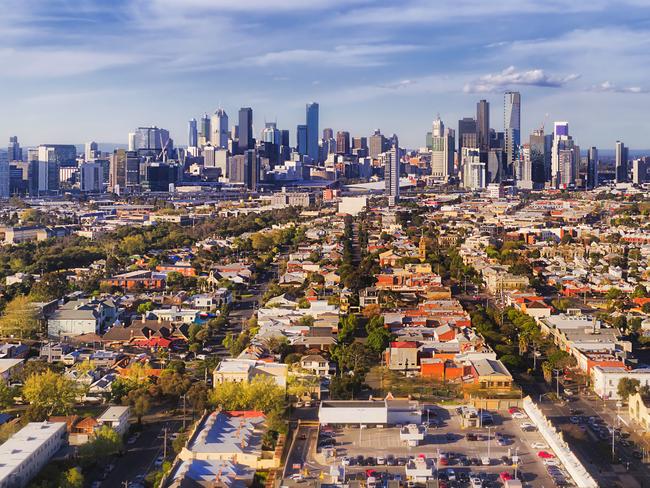 Aerial view of Melbourne city CBD high-rise towers from Port Melbourne and Southbank above residential suburb house roofs and local streets, roads, cars and parks.