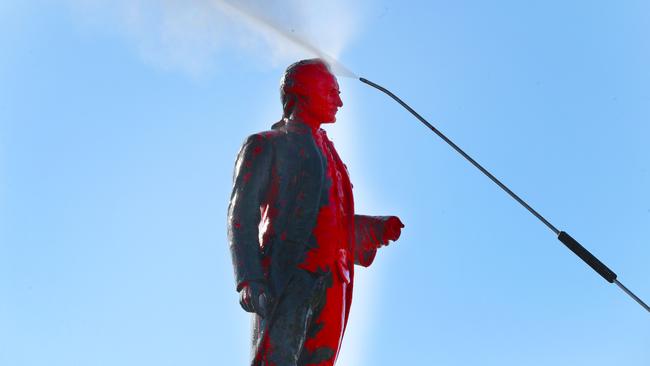 Workers use a pressure hose to get red paint off a vandalised Captain James Cook statue in Melbourne. Picture: NCA NewsWire / David Crosling