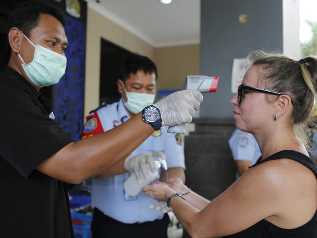 An immigration officer checks the body temperature of a foreign tourist, while another sprays hand sanitiser. Picture: AP