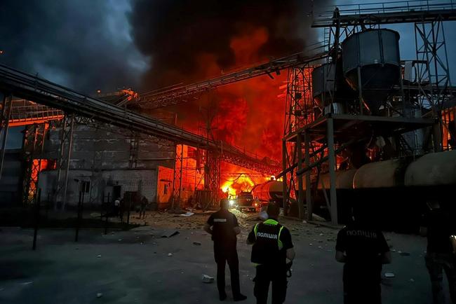 Ukrainian law enforcement officers stand next to the burning industrial facility following a missile strike in the Poltava region