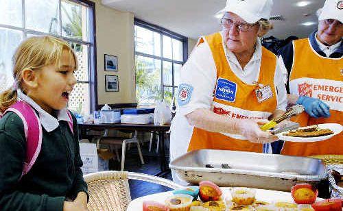 Storm victim Arancaria Velasco, 8, of Lennox Head, is served breakfast by Salvation Army volunteers June Lock (left) and Wilma Grace at the Lennox Head Bowling Club emergency centre before leaving for school. . Picture: Jay Cronan