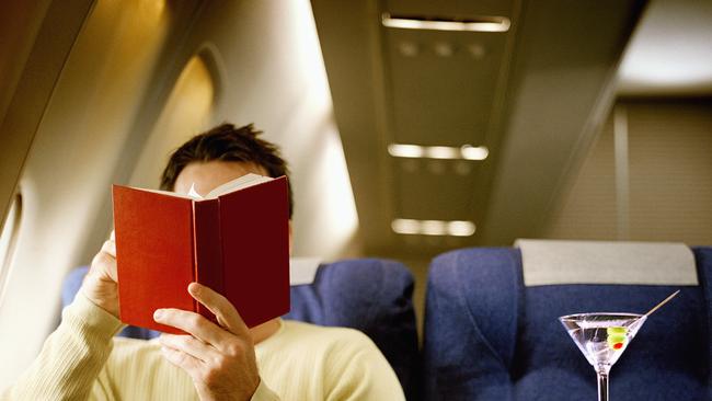 Man reading book, being served martini, in first class on airliner