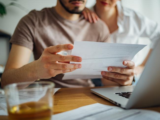 Close up photo of male hands holding bill and pen and female hands hugging him while they doing home finances together online on a laptop computer and drinking cup of tea in the kitchen.