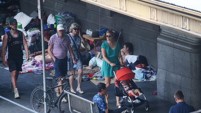 People walk past homeless people camped next to Flinders St station. Picture: Ian Currie