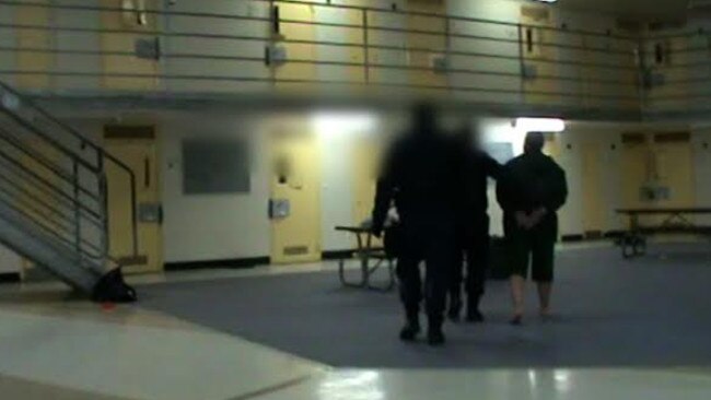 Corrective Services officers take an inmate off as they search the cell involved in the video.