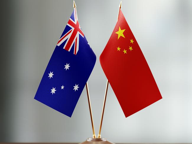 Australian and Chinese flag pair on desk over defocused background. Horizontal composition with copy space and selective focus.