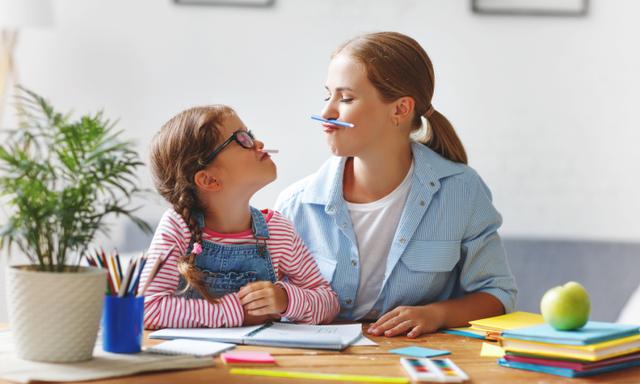 funny mother and child daughter doing homework writing and reading at home