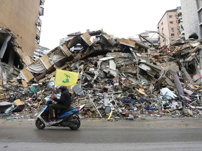 A man waves the flag of Hezbollah as he drives past the rubble of a building in Beiru as people returned to the area to check their homes after a ceasefire between Israel and Hezbollah took effect. Picture: AFP