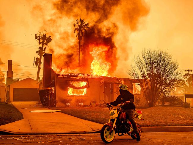 A motorcyclist stops to look at a burning home during the Eaton fire in the Altadena area of Los Angeles county, California on January 8, 2025. Terrified residents caught in blazing neighbourhoods, influencers ignoring the ban on drones and the frightening unpredictability of the wildfires are just some of what journalists covering the fires ravaging Los Angeles for AFP have had to manage. The United States' second-largest city has never faced a blaze of this scale, driven by an extreme autumn drought and fierce Santa Ana winds -- the strongest since 2011 -- that have turned dry hills into kindling, fuelling a relentless inferno that has raged for more than a week. (Photo by JOSH EDELSON / AFP)