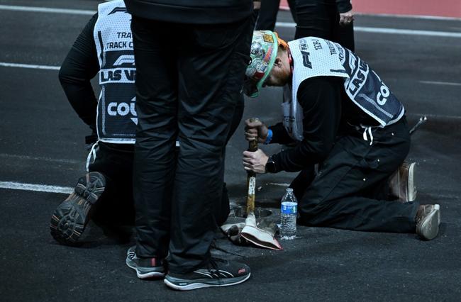 A work crew hammers in sand used to fill a drain hole on the track after trouble with the drain cover halted the first practice session for the Las Vegas Formula One Grand Prix