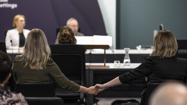 Two members of the public listening to the inquiry hold hands during Marcia Neave's opening address. Picture: ABC News: Luke Bowden