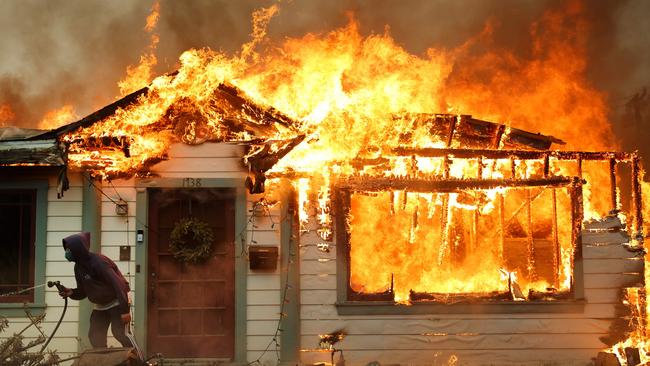 A person uses a garden hose in an effort to save a neighbouring home from catching fire during the Eaton Fire. Picture: AFP