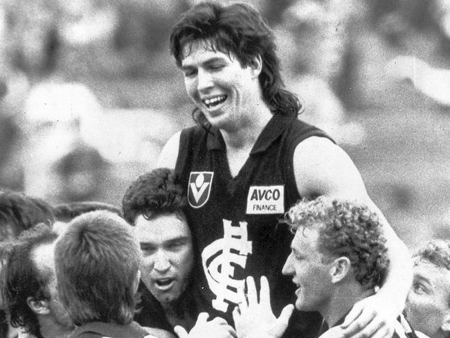 Carlton players swamp Stephen Kernahan and lift him — and his hair — from the ground.