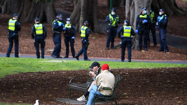 A couple enjoy a break while police patrol Treasury Gardens. Picture: AFP