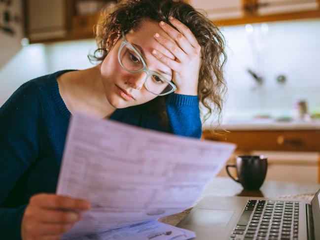 Young brunette curly female reading her bill papers, looking stressed. Picture:  iStock.