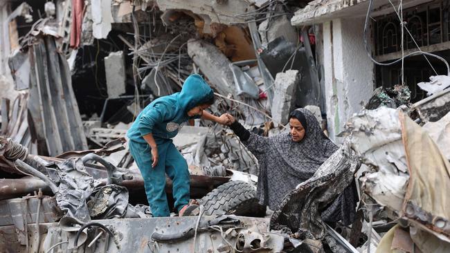 A Palestinian woman assists a child playing on the ruins of a building destroyed by the Israeli bombardment in Gaza City on Monday. Picture: AFP