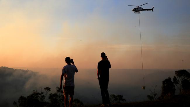 Locals take photos as helicopters water bomb at Alfords Point and Menai on Sunday. Picture: Damian Shaw