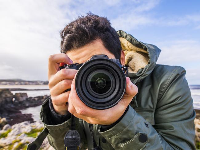 A young man using a DSLR camera at the sea