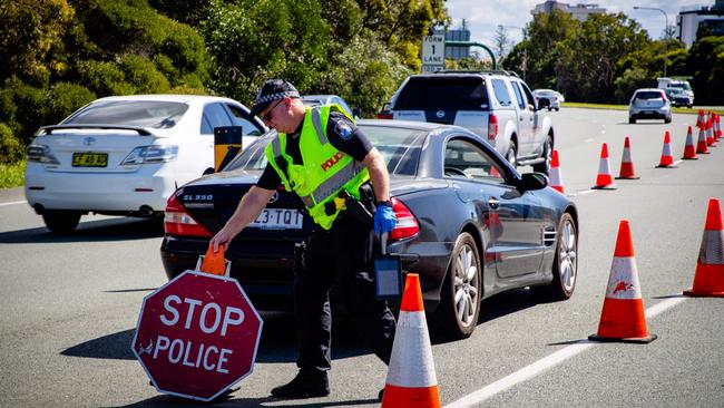 A Queensland police officer moves a stop sign at a vehicle checkpoint on the Pacific Highway on the Queensland - New South Wales border (Photo by Patrick HAMILTON / AFP)