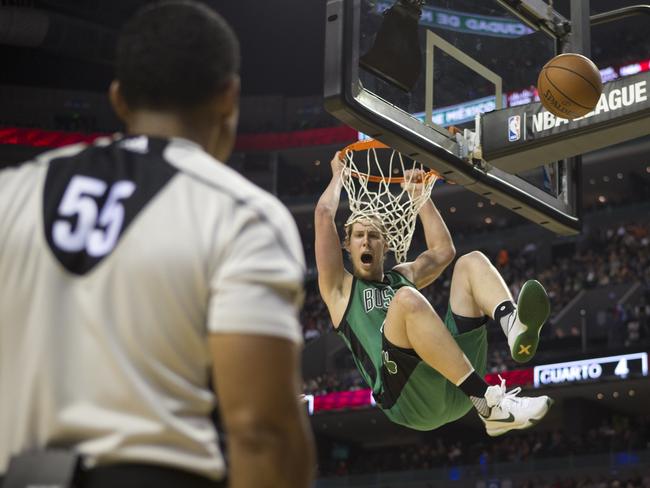 A referee watches as Boston Celtic Kelly Olynyk swings from the basket after dunking.