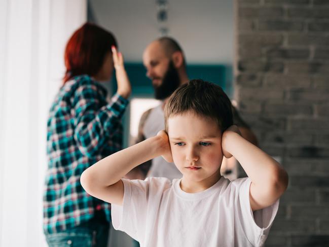 Sad child covering his ears with hands during parents quarrel. Man about to beat his wife