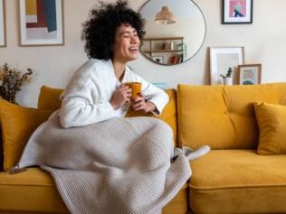 Happy African american woman enjoying quiet time at home laughing and drinking morning coffee sitting on sofa. Copy space. Lifestyle concept.