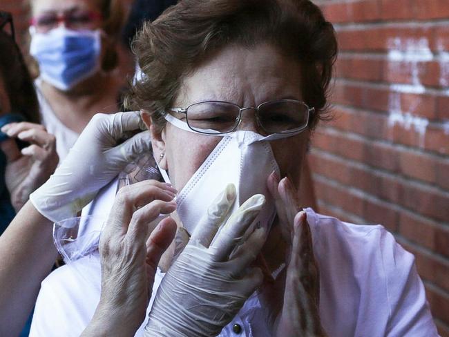 TOPSHOT - A municipal worker puts a protective face mask to a woman to prevent the spread of the new Coronavirus, COVID-19, before she visits a market, in Caracas, on March 15, 2020. (Photo by CRISTIAN HERNANDEZ / AFP)