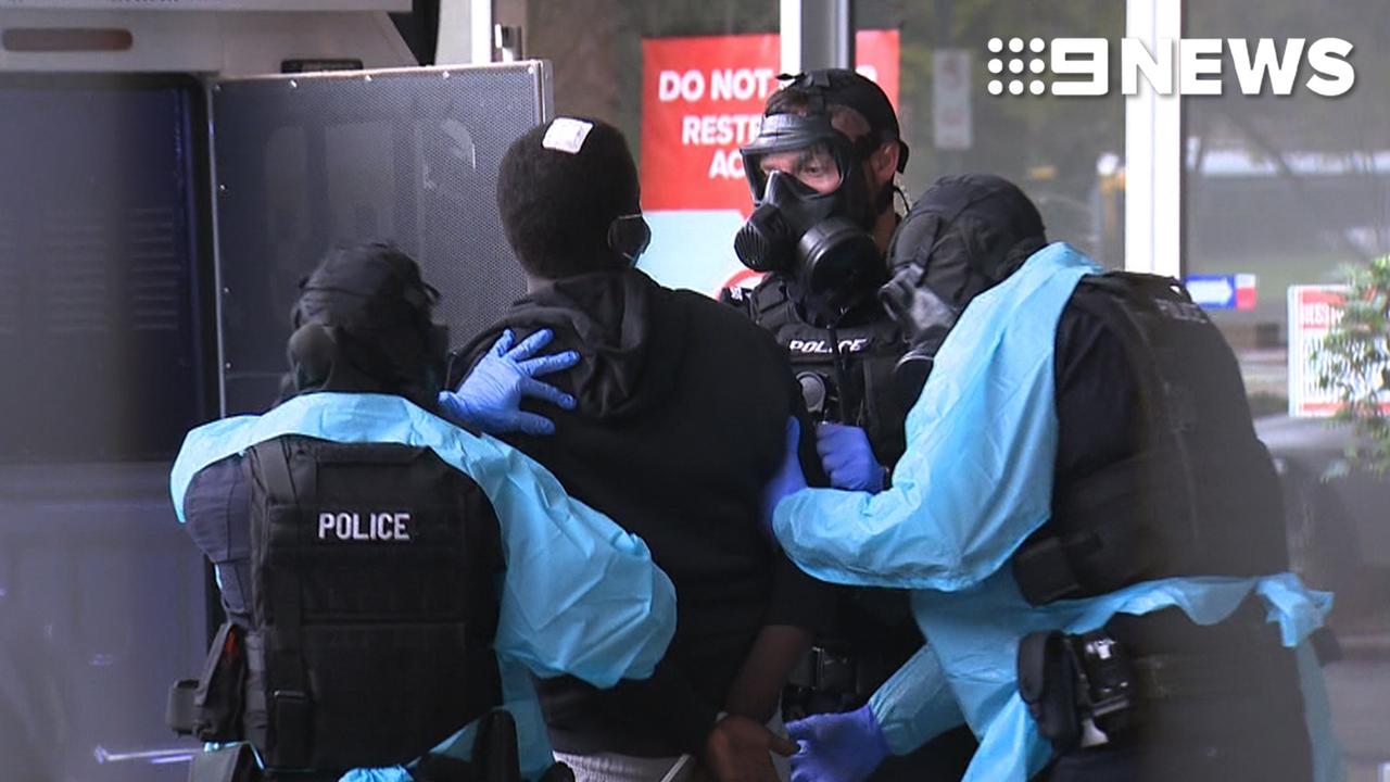 SA Police in gas masks escort a Victorian man from an Adelaide medi-hotel.