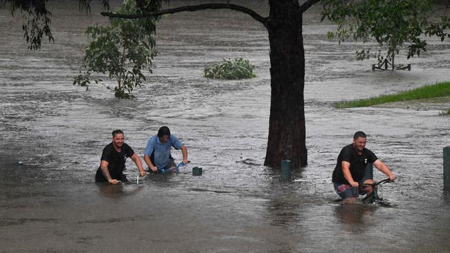 Residents attempt to ride bikes along the flooded banks of the Nepean river in Penrith on Sunday. Picture: AFP