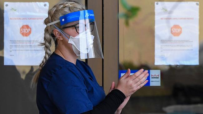 A staff member sanitises her hands outside the Menarock Life aged care facility, where a cluster of some 28 new infections had been reported today. Picture: William West/AFP