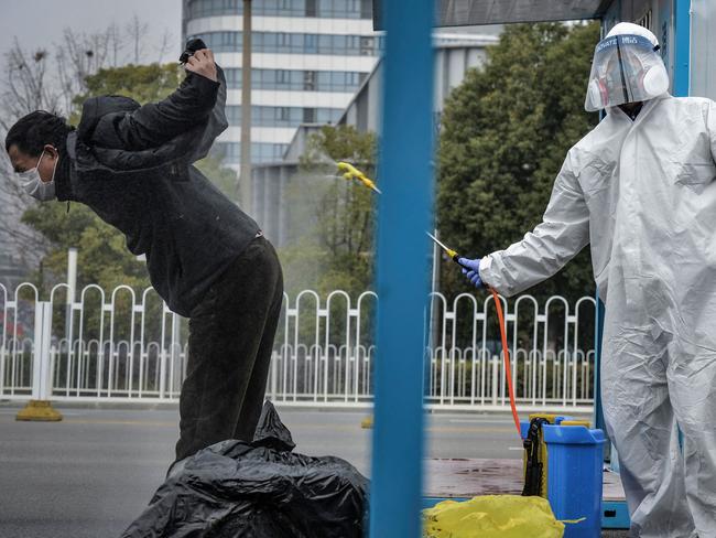 (FILES) This photo taken on February 22, 2020 shows a man (L) who has recovered from the COVID-19 coronavirus infection being disinfected by a medical staff before leaving the hospital in Wuhan in China's central Hubei province. Five years since Covid-19 started upending the world, the virus is still infecting and killing people across the globe -- though at far lower levels than during the height of the pandemic. Here is the current state of the play. (Photo by AFP) / China OUT