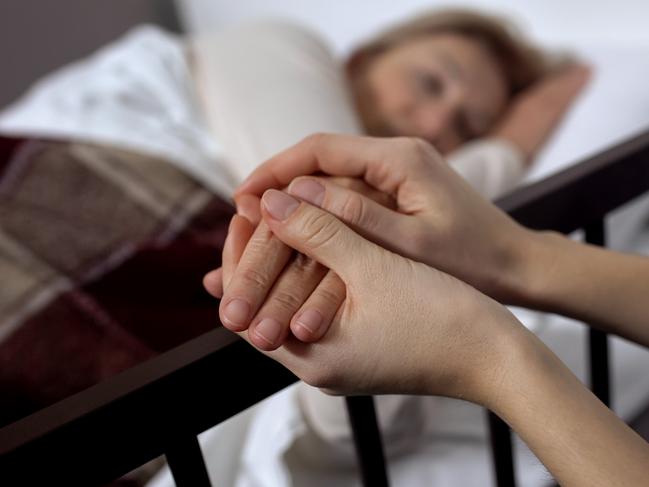 Daughter supporting her terminally ill mother lying on hospital bed, hospice istock image