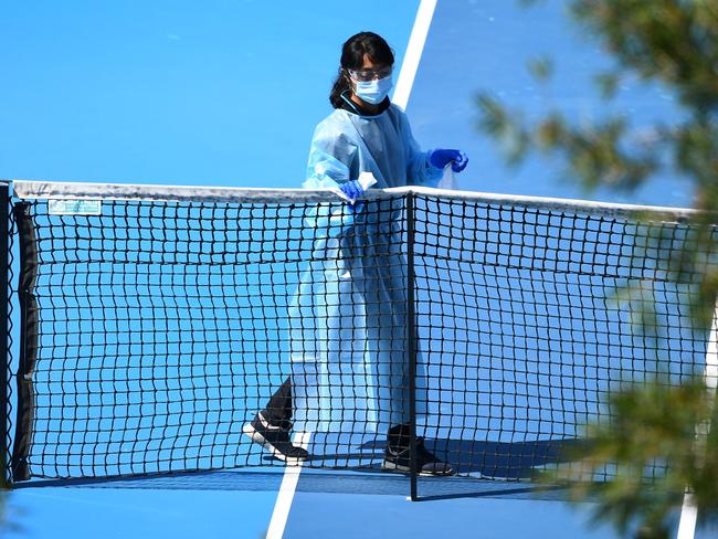 A cleaner wipes down the nets as she prepares the court for the next group of tennis players for a practice session in Melbourne on January 21, 2021, with players allowed to train while on quarantine for two weeks ahead of the Australian Open tennis tournament. (Photo by William WEST / AFP)