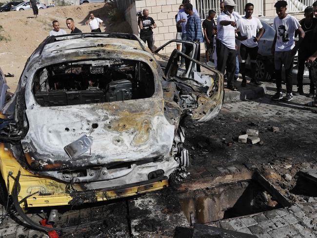 Onlookers gather around charred vehicles hit by rockets launched by Hamas militants from the Gaza Strip in the southern Israeli city of Ashkelon on the border with the Palestinian coastal enclave on May 16, 2021. (Photo by JACK GUEZ / AFP)