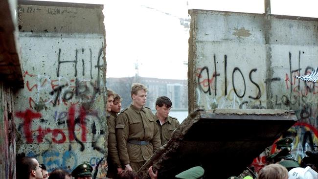 East German border guards look through hole in Berlin Wall after demonstrators pulled down segment at Brandenburg Gate on November 11, 1989.