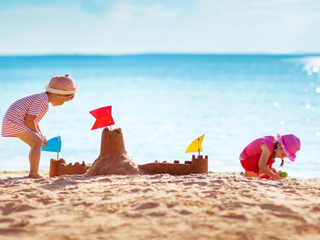 Ultimate list for family fun in Adelaide. Boy and girl playing on the beach on summer holidays. Children building a sandcastle at sea.