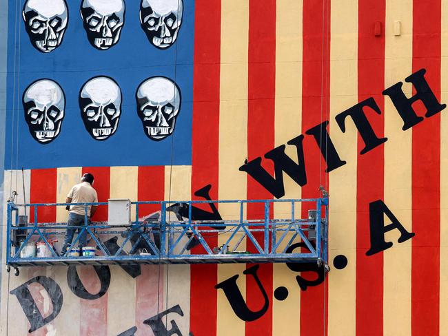 TOPSHOT - A man on a platform applies a fresh coat of paint to the landmark anti-US mural drawn on the wall of a building on Karim Khan Zand Avenue in Tehran on April 8, 2025 with the slogan 