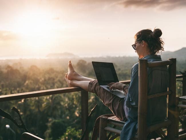 Young business woman working at the computer in cafe on the rock. Young girl downshifter working at a laptop at sunset or sunrise on the top of the mountain to the sea, working day.