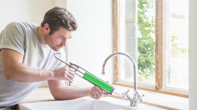 A handyman applies caulk to a kitchen in a new home.