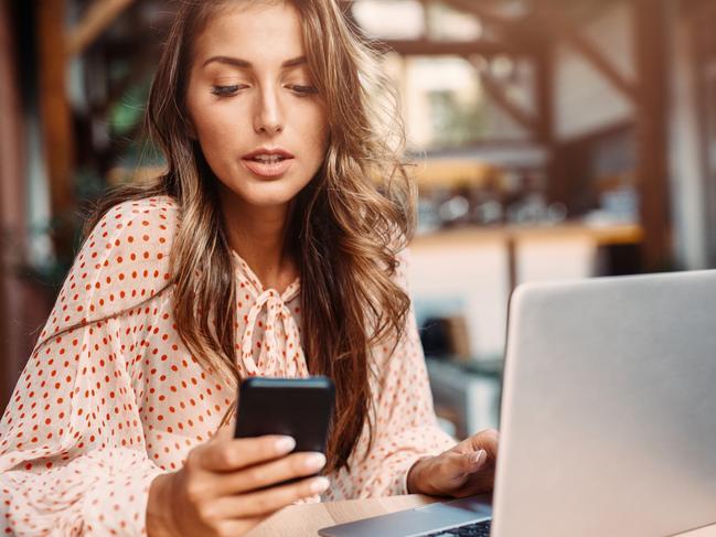 A woman on her computer using her phone reviewing her home loan. Picture: iStock.