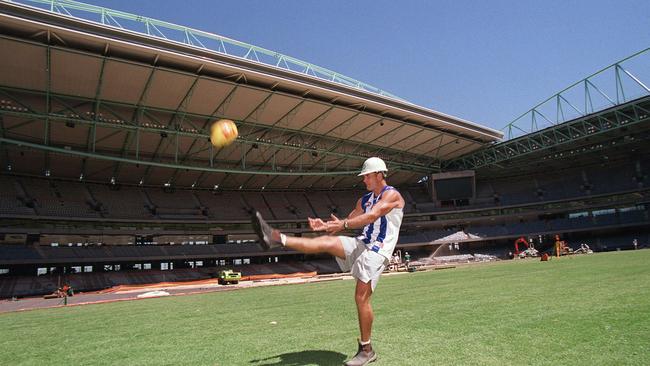 Wayne Carey with a hard hat on, kicking a ball at Docklands.